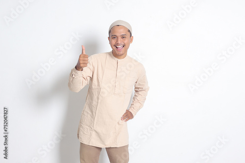 Portrait of attractive Asian muslim man in koko shirt showing thumb up, good job hand gesture. Approval concept. Isolated image on white background