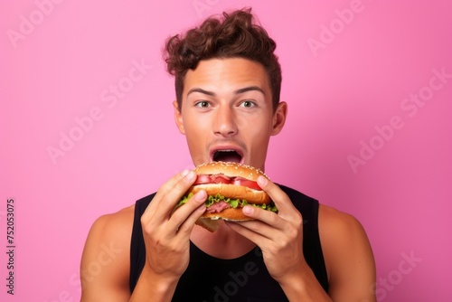 A young man holding a large hamburger in front of his face. Perfect for food and fast food concepts