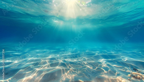 Seabed sand with blue tropical ocean above and sunny blue sky, empty underwater background with the sun shining brightly, creating ripples in the calm sea water