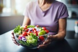 Woman holding bowl of vegetables on table. Suitable for healthy eating concept