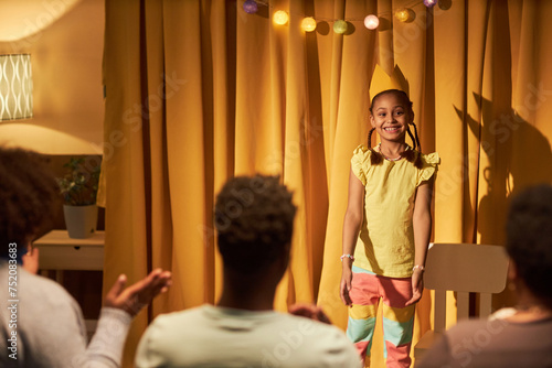 Portrait of smiling Black little girl standing on stage in makeshift theater and wearing princess crown, copy space