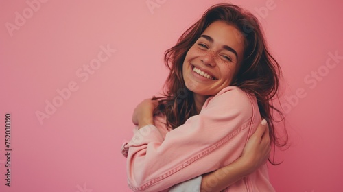 Stunning brunette in casual attire on pink backdrop embracing herself with a joyful and self-assured smile, promoting self-love and self-care. photo