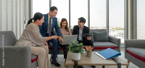 A group of business professional gathered around a small table in a modern office setting with large window that let in natural light. Young woman engaged in a discussion or presentation in a meeting.