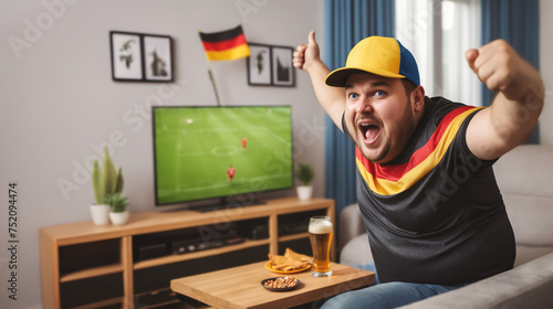 Excited German soccer fan watches a European soccer match on the TV in his living room. He has happy emotions and strikes a winning pose. He is 30 years old and wearing a soccer jersey.
