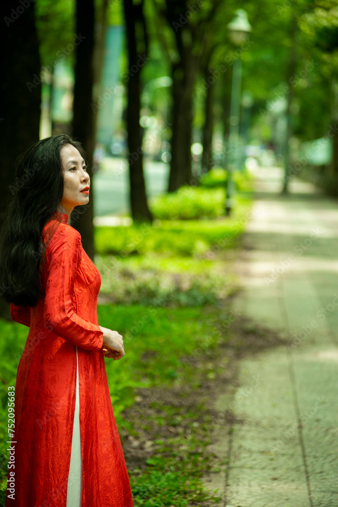 Woman wearing traditional Vietnamese ao dai walking on the road of flying tamarind leaves.Portrait of woman wearing black sunglasses while standing behind friend. Woman wearing traditional Vietnamese ao dai walking on the road of flying tamarind leaves.Portrait of woman wearing black sunglasses while standing behind friend.