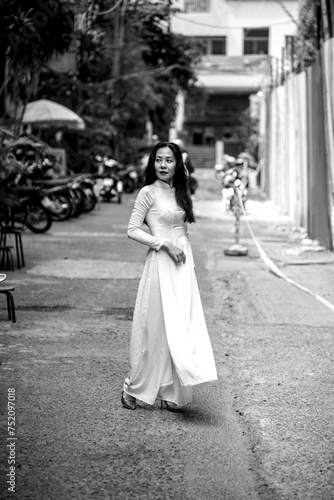 Woman wearing traditional Vietnamese ao dai walking on the road of flying tamarind leaves.Portrait of woman wearing black sunglasses while standing behind friend.