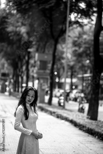 Woman wearing traditional Vietnamese ao dai walking on the road of flying tamarind leaves.Portrait of woman wearing black sunglasses while standing behind friend. © Mr duolingo