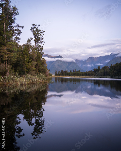 Beautiful lake surrounded by exotic forest and mountains in background during sunset, New Zealand