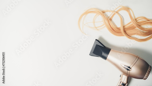 Piece of wavy blonde hair and a  hair dryer with copy space on the white background. Hairdresser concept.