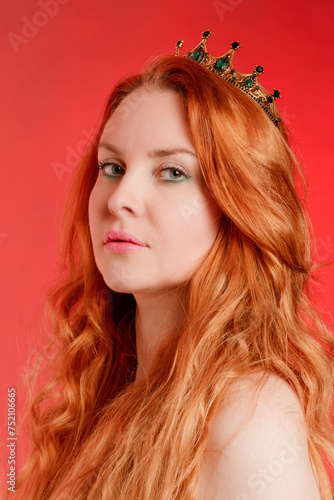 Portrait of a red-haired young woman with a crown on her head on a scarlet background