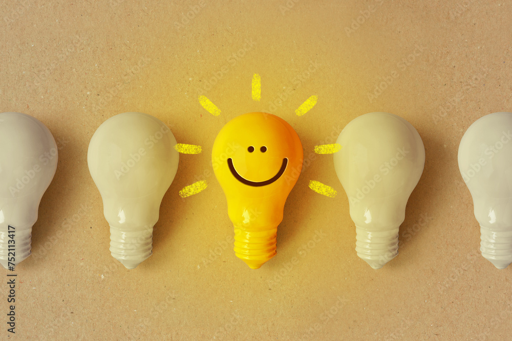 Glowing yellow light bulb with smile and white light bulb turned off - Positive thinking and standing out from crowd concept - obrazy, fototapety, plakaty 