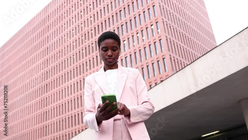 Young african businesswoman using a phone in finantial district. Young successful black businesswoman working in the street photo