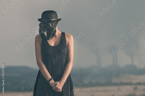 young girl in a black dress and gas mask on the background of smoking factory chimneys in Ukraine close up