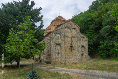 Two tiled domes, arched walls of Gurjaani Kvelatsminda Church, Georgia. Trees and bushes around. Clear sky with clouds. photo