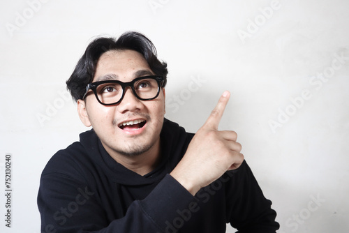 Adult Asian man wearing black hoodie pointing behind him.