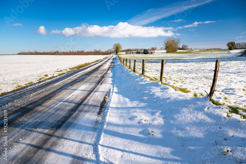 Paysage d'hiver. Route de campagne enneigée avec verglas à travers prairies et champs photo