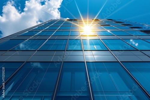 office building with a reflective glass facade under a clear blue sky with the sun shining brightly.