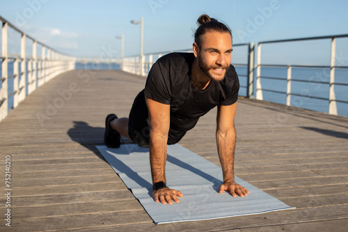 Young European sportsman in sportswear holds a plank position outdoors
