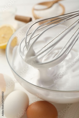 Bowl with whipped cream, whisk and ingredients on white wooden table, closeup