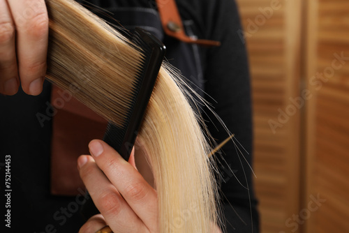 Hairdresser combing client's hair in salon, closeup