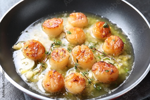 Delicious scallops with sauce in frying pan on table, closeup