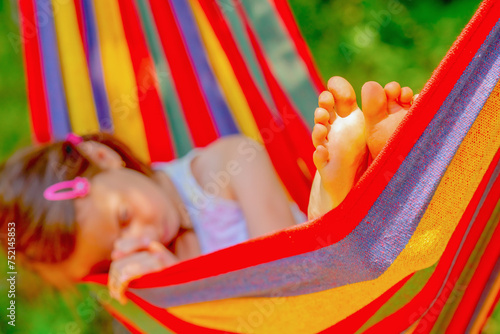 Young beautiful girl sleeping in a hammock with bare feet, relaxing and enjoying a lovely sunny summer day. Safety and happy childhood and leisure concept. Selective focus on bare feet