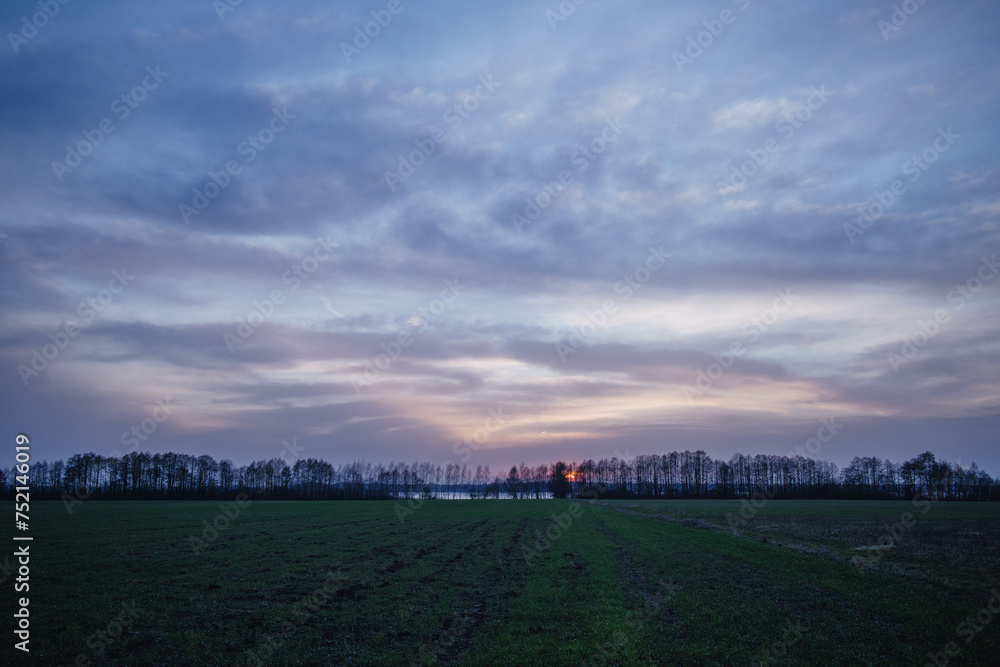 sunset over the field with mamry lake in the background sunset over the field with mamry lake in the background