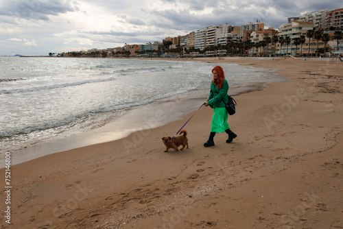 Paisaje maritimo con señora vestida de verde paseando a la perrita Nami en la playa de Villajoyosa, España photo