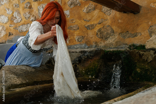 Mujer con vestido de epoca modernista lavando la ropa en lavadero antiguo de la población de Sella, España photo