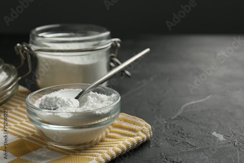 Baking powder in bowl, jar and spoon on black textured table, closeup. Space for text