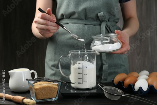 Woman adding baking powder into measuring cup at black wooden table  closeup