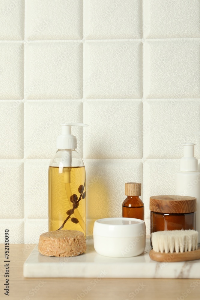 Different bath accessories and personal care products on wooden table near white tiled wall, space for text