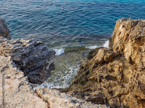 View from above over beautiful turquoise waves of blue Mediterranean Sea coming on rough yellow and orange porous rocks in Ayia Napa, Cyprus.