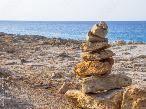Stone tower of rough yellow and orange porous rocks piled on the shore of the blue Mediterranean sea in Ayia Napa, Cyprus.