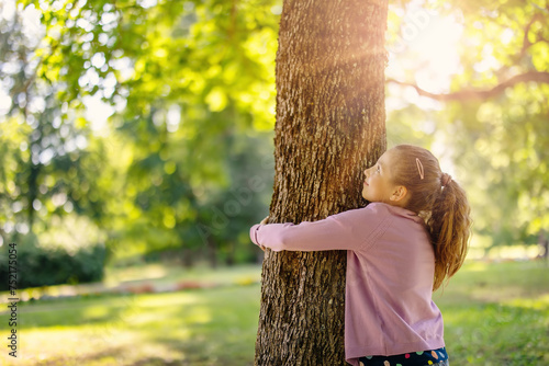 Cute little girl hugging tree in the natural park.