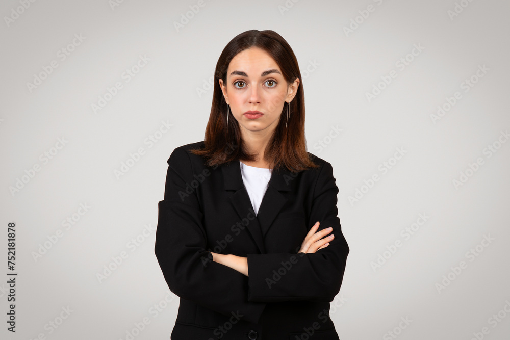 Confident young businesswoman with long brown hair and a black suit stands with crossed arms Confident young businesswoman with long brown hair and a black suit stands with crossed arms