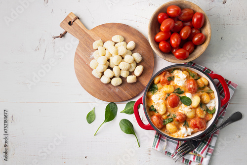 Creamy gnocchi with tomato sauce, spinach and mozzarella on a white wooden table