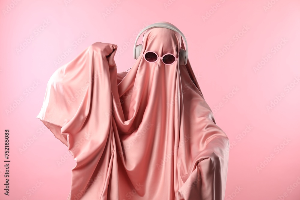 Glamorous ghost. Woman in sheet with sunglasses and headphones on pink background Glamorous ghost. Woman in sheet with sunglasses and headphones on pink background