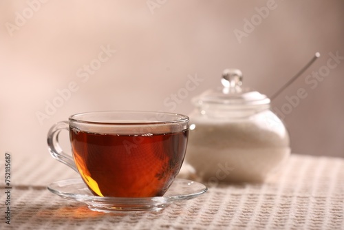 Aromatic tea in cup, saucer and sugar on table