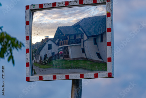 Reflections of residential buildings in traffic mirror at rural village of Sutna on a cloudy summer evening. Photo taken August 10th, 2023, Šutna, Slovenia. photo