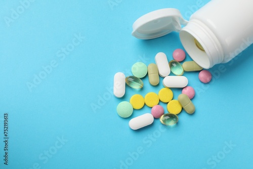 White bottle and different vitamin pills on light blue background, above view. Space for text