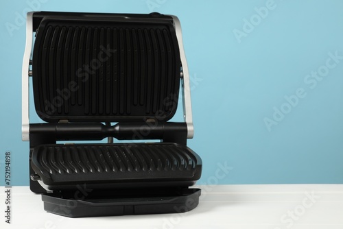 Electric grill on white wooden table against light blue background, space for text. Cooking appliance