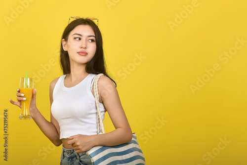 Cute pretty girl with a striped bag on her shoulder holding a glass with a delicious soft drink on a yellow background. Young beautiful brunette resting on a sunny summer day photo