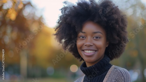 Close-up portrait of an attractive young African American woman wearing warm knitted sweater posing outdoors. Cheerful smiling black female model in autumn park.