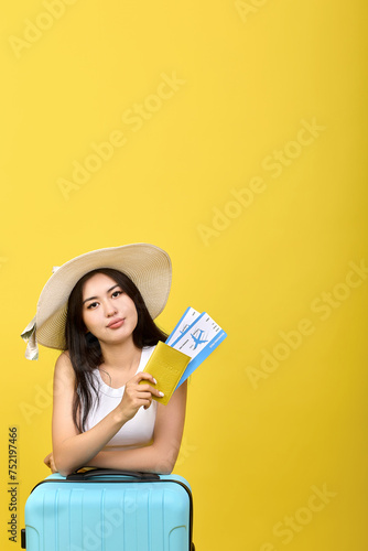 Beautiful young tourist in a hat holds a passport and plane tickets for a summer vacation in her hand. Successful self-confident young woman posing on yellow background before flying on a trip