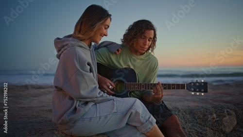 Smiling couple play guitar music at sundown seashore. Relaxed woman singing song