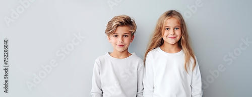 Brother and sister in light clothes, children standing next to each other and smiling, empty space for text, national siblings day, banner. Portrait of cute children on a light background