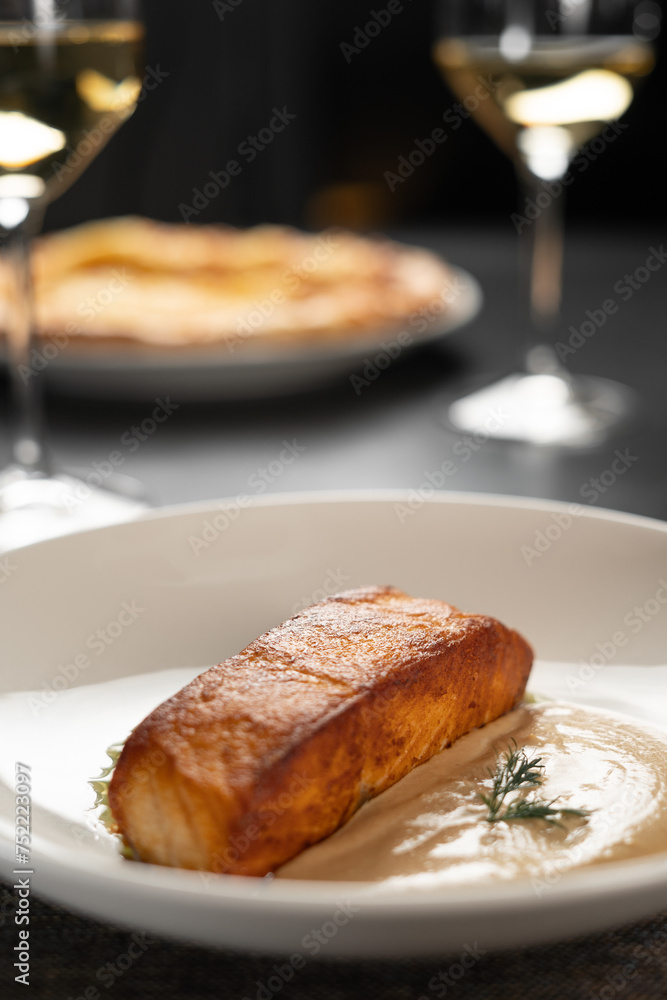 Delicious salmon filet with two sauce on a white plate serving with wine in restaurant. Healthy seafood meal