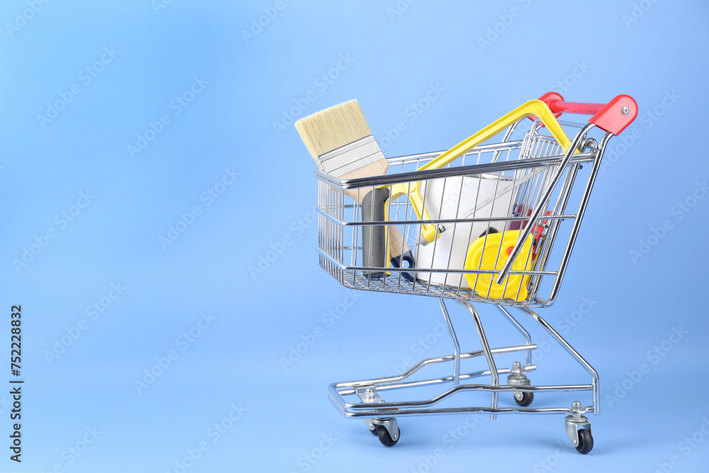 Small shopping cart with paint and renovation equipment on light blue background. Space for text