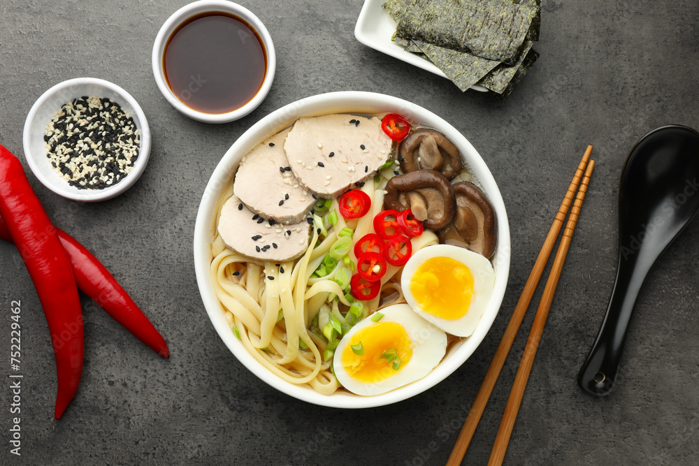 Delicious ramen with meat in bowl and ingredients on grey textured table, flat lay. Noodle soup